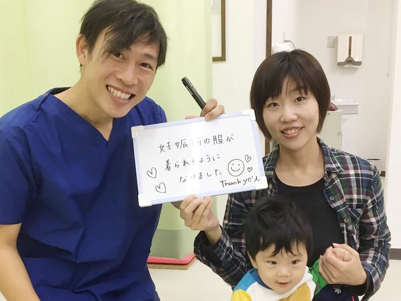 ご来院いただいた方と院長の写真。ボードに「妊娠前の服が着られるようになりました」