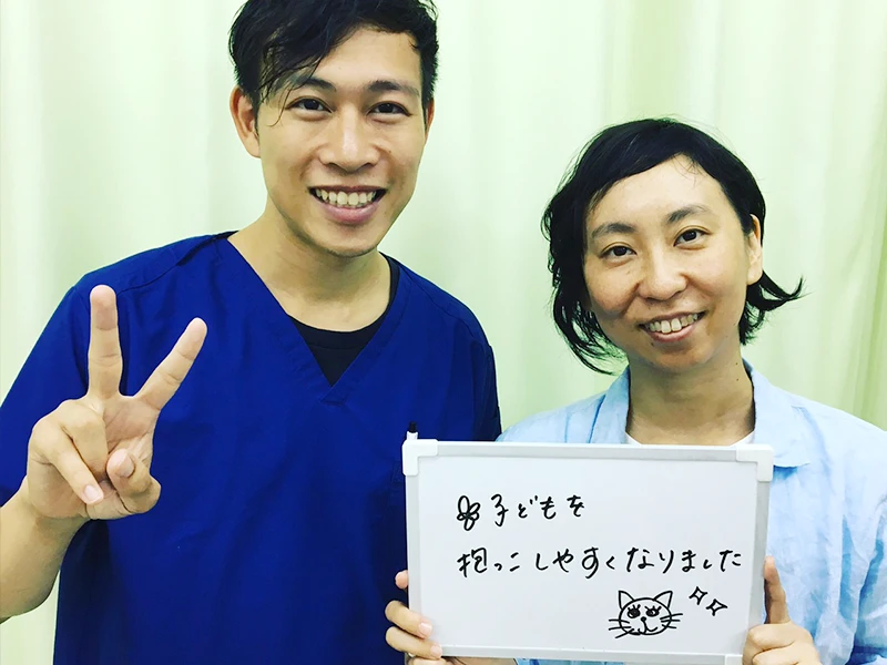 ご来院いただいた方と院長の写真。ボードに「子どもを抱っこしやすくなりました」